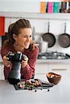 A woman photographer is leaning on a modern kitchen counter. Seh is laughing, taking a break from photographing autumn fruits and vegetables - mushrooms, garlic, rosemary, and cranberries.