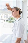 Confident female doctor looking through windows in hospital