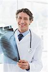 Happy doctor holding X-ray and smiling at camera in medical office