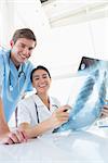 Happy doctors looking at camera and holding X-ray in medical office