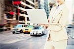 Confident businesswoman holding laptop against new york street