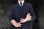 Smiling businessman in suit with arm out against black background