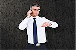 Businessman on the phone looking at his wrist watch against grey background