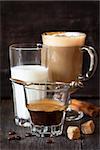 Glass of hot espresso, sprinkled with grated chocolate latte and whipped milk on wooden board close up.