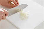 Close up of woman's hands slicing onions with a kitchen knife