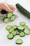 Close up of woman's hands slicing cucumbers with a kitchen knife