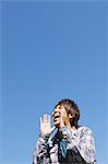 Young man shouting against blue sky