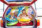 Child poses with his dog in the open trunk of a car full of beach toys and floaties