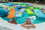 Two children wearing scuba masks and snorkels swim in a pool full of inflatable toys