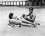 1930s 1940s COUPLE WEARING BATHING SUITS SITTING  RELAXING POOL SIDE DRINKING BEER