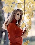 1970s PORTRAIT SMILING LONG HAIR BLOND WOMAN LOOKING AT CAMERA IN AUTUMN TREE LEAVES