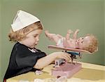 1960s LITTLE GIRL DRESSED IN NURSE'S COSTUME WEIGHING HER DOLL ON TOY BABY SCALE