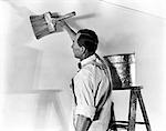 1930s 1940s MAN IN WHITE OVERALLS BY STEP LADDER ZINC PAIL BUCKET APPLYING PAINT GLUE WITH LARGE BRUSH TO PREPARE FOR WALLPAPER