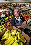 A man standing in a grocery shop beside a display of fresh fruits and vegetables.