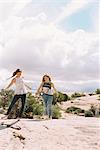 Two women running barefoot across the sand in a desert landscape