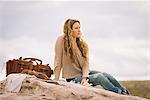 Woman sitting on a rock in a desert, a leather bag standing beside her.