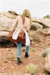Woman walking past rocks in a desert, carrying a leather bag.