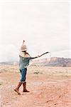 A woman with her arms raised, hitting a stone with a stick into the distance.