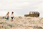 Two women walking towards a 4x4 parked in a desert.