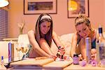 Two young women having girls night in, sitting on sofa, painting toes