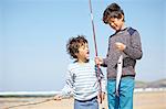 Two young boys standing together, holding fishing rod and fish