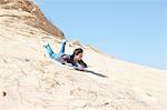 Young boy, sledging down sandy hill