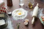 Table with raw egg in center of flour stack and kitchen utensils