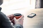 Over shoulder view of man drinking coffee with smartphone on desk