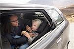 Mother adjusting son's seatbelt in car