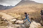 Woman leaping over stream, Fairy Pools, near Glenbrittle, Isle of Skye, Hebrides, Scotland