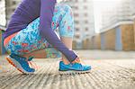 Cropped view of woman bending to tie sports training shoe lace