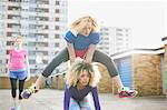 Three women exercising together wearing sports clothing and playing leap frog