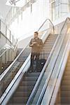 Young businessman commuter on escalator with suitcase.
