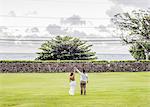 Rear view of bride and bridegroom holding raised hands in garden at Hawaiian wedding, Kaaawa, Oahu, Hawaii, USA