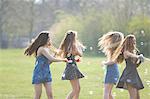 Four teenage girls spinning bubbles with bubble wand in park