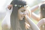 Portrait of teenage girl putting on daisy chain headdress in park