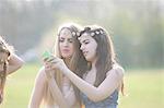 Two teenage girls wearing daisy chain headdresses reading smartphone texts in park