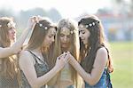 Four teenage girls wearing daisy chain headdresses reading smartphone texts in park