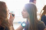 Teenage girl having lipstick applied by best friend in bedroom