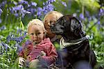 Young boy sitting with baby sister and dog in bluebell forest