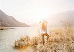 Rear view of young woman practicing yoga on lakeside, Lake Mergozzo, Verbania, Piemonte, Italy