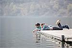 Young couple lying on pier dipping fingers in Lake Mergozzo, Verbania, Piemonte, Italy