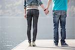 Cropped rear view of young couple holding hands on pier at Lake Mergozzo, Verbania, Piemonte, Italy