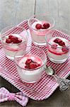 Glasses of vanilla yoghurt and raspberries on gingham tray