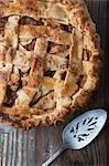 An apple pie on a wooden surface with a cake slice