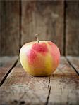 A red and yellow apple on an old, brown wooden surface in front of a wooden wall