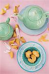 Pastel blue tea crockery, a teapot and broken fortune cookies on a pink tablecloth