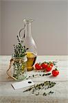 A bottle of olive oil, thyme and cherry tomatoes on a light wooden surface