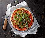 Pizza Margherita with rocket on a piece of paper with a knife