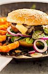 A hamburger with grilled portobello mushrooms, baby chard, onions, Camembert and chips